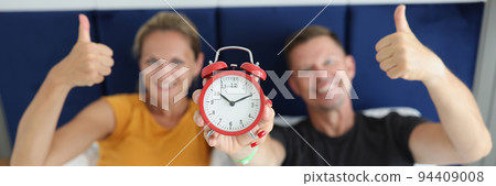 Married couple is holding alarm clock and thumbs up gesture 94409008