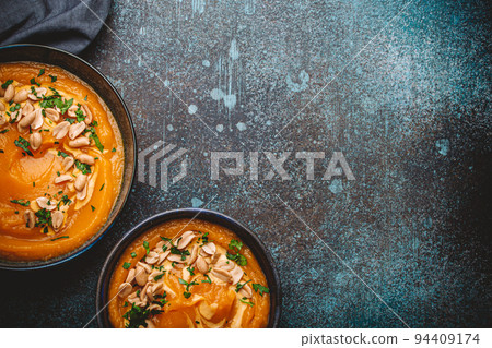 Bowl with pumpkin cream soup with peanuts on dark stone background Bowl with pumpkin cream soup with peanuts on dark stone background 94409174