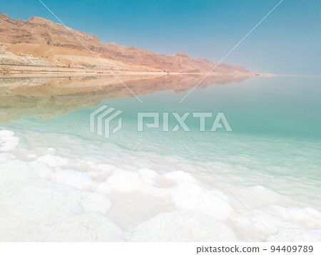 Landscape view on Dead Sea salt crystals formations, clear cyan green water and mountains at Ein Bokek beach, Israel 94409789