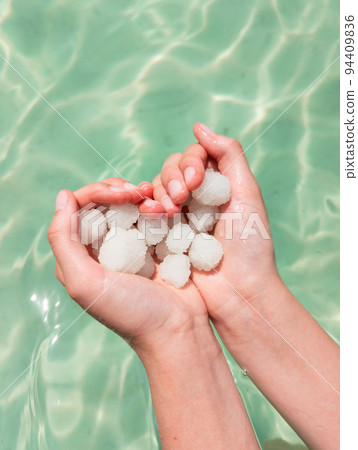 Hands holding sea salt crystals heart-saped on sea water background 94409836