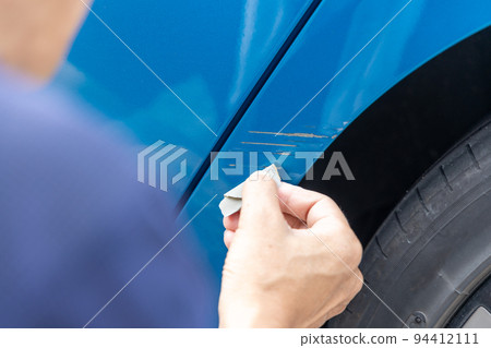 Hands of a senior man trying to repair scratches on the body of a blue car by himself 94412111