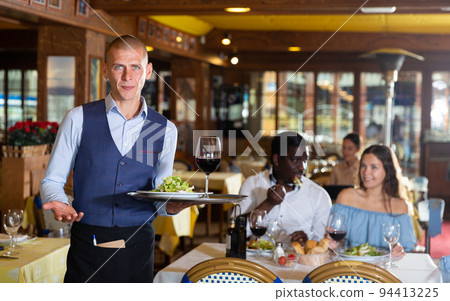 Waiter standing with serving tray, recommending dishes in restaurant 94413225