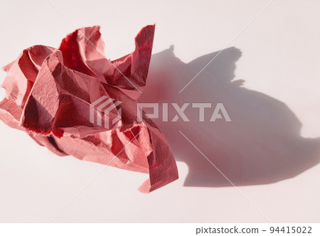 A crumpled paper ball made of pink paper and its shadow on a light background, top view 94415022