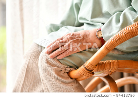 Senior woman in an apron sitting on a rattan chair Senior woman in an apron sitting on a rattan chair 94418786