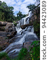 Beautiful flowing water of Mae Klang waterfall located in Chom Thong district, Chiang Mai, northern of Thailand. Surrounded with many trees in the forest with blue sky and white cloud as background. 94423089