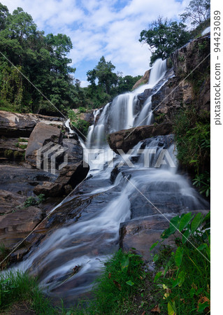 Beautiful flowing water of Mae Klang waterfall located in Chom Thong district, Chiang Mai, northern of Thailand. Surrounded with many trees in the forest with blue sky and white cloud as background. Beautiful flowing water of Mae Klang waterfall located in Chom Thong district, Chiang Mai, northern of Thailand. Surrounded with many trees in the forest with blue sky and white cloud as background. 94423089
