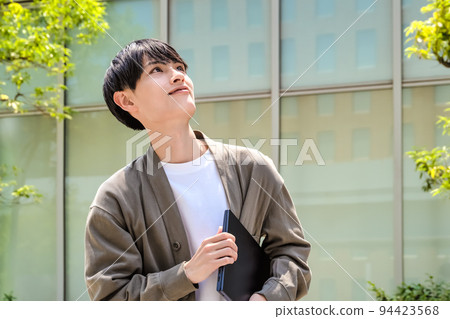 A young business man in office casuals holding a laptop looking up 94423568