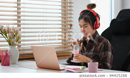 Asian woman using microphone and laptop computer recording podcast at small broadcast studio Asian woman using microphone and laptop computer recording podcast at small broadcast studio 94425288