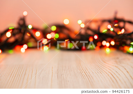 Blurred product background with Christmas New Year colorful light bulbs garland and wooden table. Selective focus, copy space for beauty product packaging, advertising backdrop. Empty place Blurred product background with Christmas New Year colorful light bulbs garland and wooden table. Selective focus, copy space for beauty product packaging, advertising backdrop. Empty place 94426175