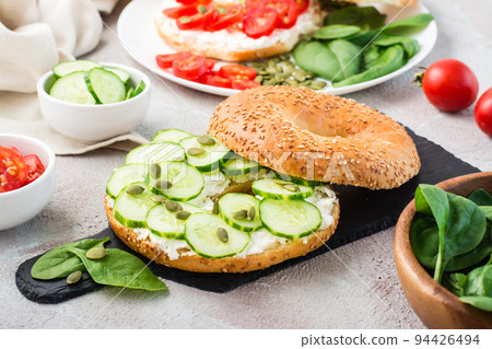 Delicious bagel stuffed with feta, cucumber and pumpkin seeds and spinach leaves on a slate board. Light Vitamin Healthy Snack. Close-up 94426494