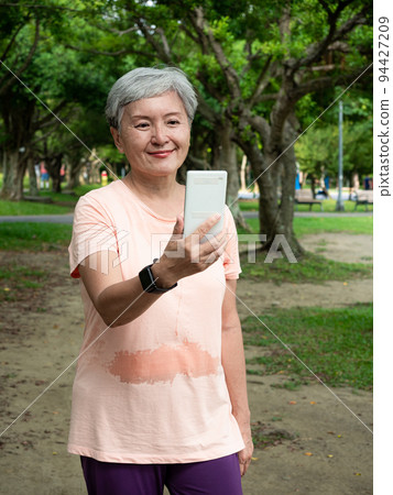 Portrait of senior adult elderly asian woman 60s smiling standing and holding smartphone in the park. Portrait of senior adult elderly asian woman 60s smiling standing and holding smartphone in the park. 94427209
