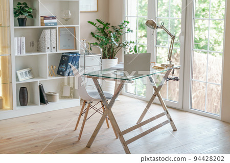 Comfortable workplace with a laptop in the office, at home. Bright room with large windows, bookcase, green plant. Remote work, freelance. 94428202