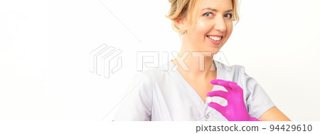Portrait of a young smiling Caucasian beautician wearing pink gloves holding sugar cubes showing and looking at the camera against a white background Portrait of a young smiling Caucasian beautician wearing pink gloves holding sugar cubes showing and looking at the camera against a white background 94429610