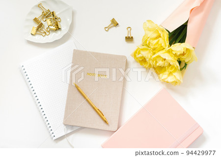 Spring Feminine workspace blogger. Notebooks with a pen, a bouquet of yellow tulips on a white background. Trendy stylish flat lay 94429977
