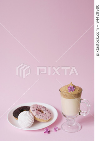 Beautiful dalgon coffee drink. A Cup of coffee with foam and lilac flower, a plate of sweets Beautiful dalgon coffee drink. A Cup of coffee with foam and lilac flower, a plate of sweets 94429980