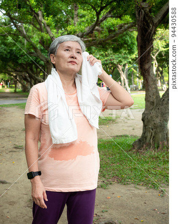 快樂的樂齡亞洲婦女微笑著站在草地上,脖子披著運動毛巾,享受公園裡的大自然新鮮空氣. 快樂的樂齡亞洲婦女微笑著站在草地上,脖子披著運動毛巾,享受公園裡的大自然新鮮空氣. 94430588