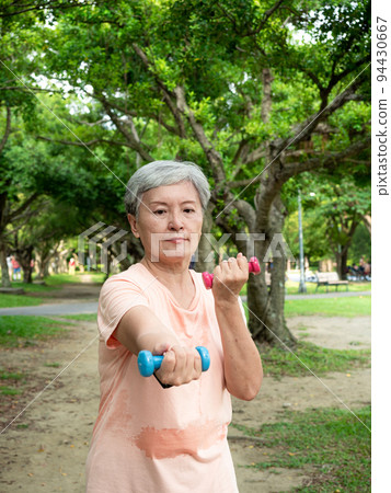 Happy senior asian woman smiling and using dumbbells while standing on grass and enjoying nature fresh air in park. Happy senior asian woman smiling and using dumbbells while standing on grass and enjoying nature fresh air in park. 94430667