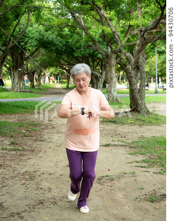 Happy senior Asian woman smiling and jogging on grass and enjoying nature fresh air in park. 94430706