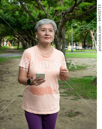 快樂的樂齡亞洲婦女微笑著草地上慢跑運動,並且享受公園裡的大自然新鮮空氣. 94430715