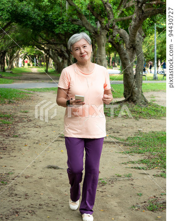 快樂的樂齡亞洲婦女微笑著草地上慢跑運動,並且享受公園裡的大自然新鮮空氣. 94430727