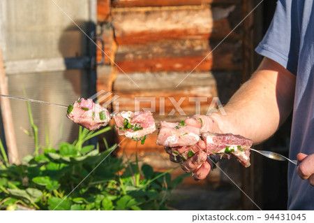 A man strands pickled meat on a skewer. A man puts A man strands pickled meat on a skewer. A man puts 94431045