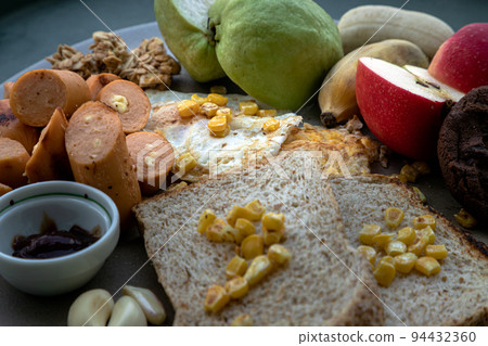 Close-up of Breakfast with Fried sausages, Fried eggs, Sweet corn kernels to put it on top Breads, Garlic, Dark chocolate cookie, Cereal, and various fresh fruits. Close-up of Breakfast with Fried sausages, Fried eggs, Sweet corn kernels to put it on top Breads, Garlic, Dark chocolate cookie, Cereal, and various fresh fruits. 94432360