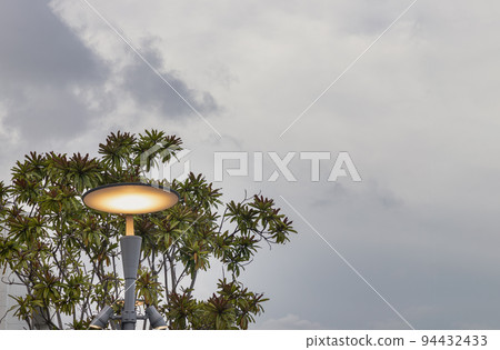 Glowing street light on Metal pole against Green bushes with Blue skies background. Glowing street light on Metal pole against Green bushes with Blue skies background. 94432433