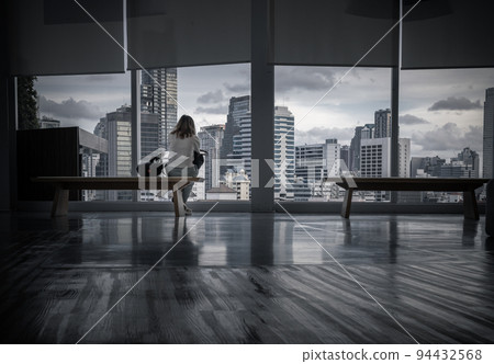 A young asia woman sitting looking through transparent wall at cityscape with skyscrapers. A young asia woman sitting looking through transparent wall at cityscape with skyscrapers. 94432568