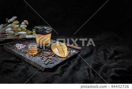 Glass of Iced tropical Mango smoothie mixed Espresso coffee served with Honey on the Wooden cutting board. 94432726