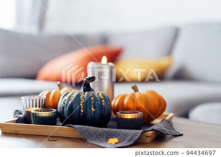 Autumn cozy mood composition for hygge home decor. Orange and gray pumpkins , burning candles on the tray with gray napkin on the coffee table in the living room. Selective focus. Copy space. Autumn cozy mood composition for hygge home decor. Orange and gray pumpkins , burning candles on the tray with gray napkin on the coffee table in the living room. Selective focus. Copy space. 94434697