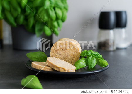 Raw Tempeh or Tempe, made of fermented soybean seeds on kitchen table. Tempeh Slices on plate with herbs. Soya protein. Plant based meat concept. Healthy eating. Go vegan. Selective focus, copy space Raw Tempeh or Tempe, made of fermented soybean seeds on kitchen table. Tempeh Slices on plate with herbs. Soya protein. Plant based meat concept. Healthy eating. Go vegan. Selective focus, copy space 94434702