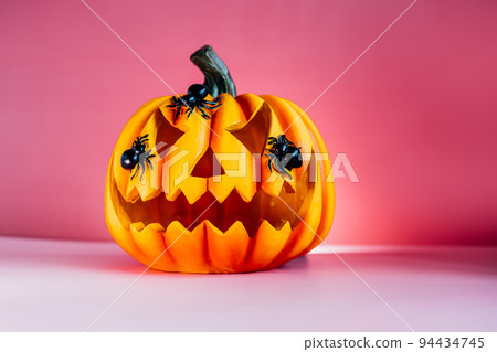 Bright pink Halloween background with carved orange pumpkin. Halloween Jack-o-lantern with spiders on it. Happy Halloween decor concept. Festive postcard with copy space. Selective focus 94434745