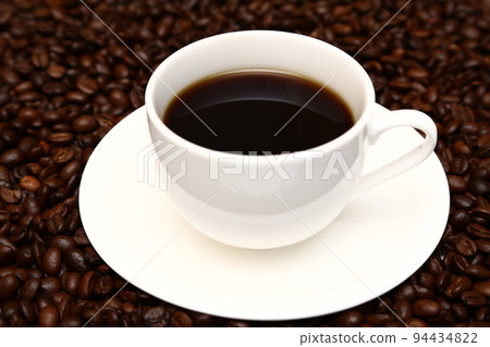 漂浮在咖啡豆上的白色杯子裡的熱咖啡 漂浮在咖啡豆上的白色杯子裡的熱咖啡 94434822