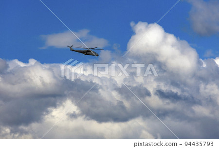 Russian combat helicopter is flying against the background of clouds in the summer sky. Russian combat helicopter is flying against the background of clouds in the summer sky. 94435793