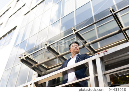 Asian businessman boss stands near his office center on the balcony in a dark color business suit Asian businessman boss stands near his office center on the balcony in a dark color business suit 94435938