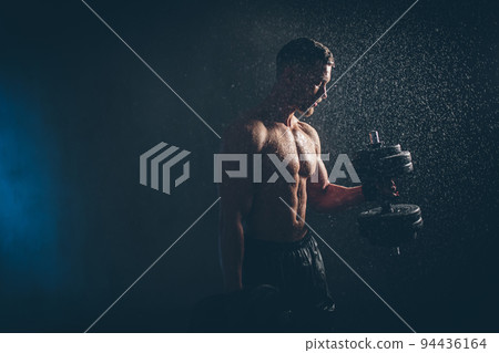 Male blond athlete lifts dumbbells with hand on biceps studio photo with raindrops Male blond athlete lifts dumbbells with hand on biceps studio photo with raindrops 94436164