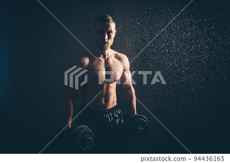 Male blond athlete lifts dumbbells with hand on biceps studio photo with raindrops Male blond athlete lifts dumbbells with hand on biceps studio photo with raindrops 94436165