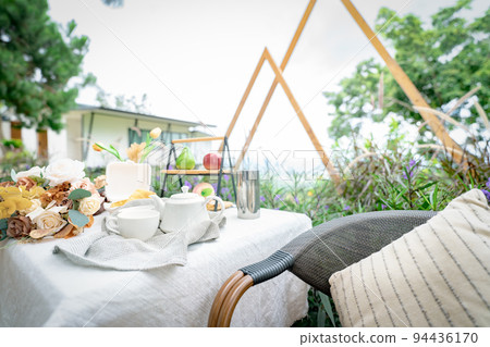 Coffee cup and flowers bouquet on table in garden. Afternoon tea concept. Home outdoor furniture. Wicker chair and table with white tablecloth in vintage style. Cozy chair and table on the terrace. 94436170