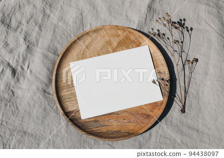Blank greeting card card mockup on wooden plate, tray. Dry grass, plant in sunlight. Beige linen background, shadow overlay. Modern template for branding identity. Autumn, winter design. Flat lay, top 94438097