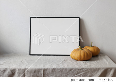 Moody autumn still life. Landscape black picture frame mockup. Orange pumpkins on linen table cloth. White wall background. Minimal rustic interior, neutral color. Halloween, Thanksgiving concept. Moody autumn still life. Landscape black picture frame mockup. Orange pumpkins on linen table cloth. White wall background. Minimal rustic interior, neutral color. Halloween, Thanksgiving concept. 94438109