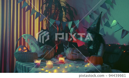 Two girls and a guy in creepy Halloween costumes are sitting at a table and taking the pulp out of pumpkins Two girls and a guy in creepy Halloween costumes are sitting at a table and taking the pulp out of pumpkins 94439981