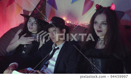 A group of friends are watching a Halloween movie on TV, laughing and chatting together 94439997