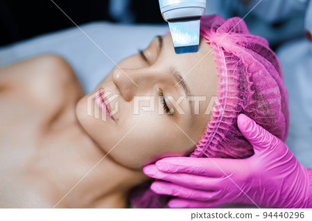 Beautician cosmetologist doing ultrasonic facial cleansing skin with device, professional cosmetic procedure in a beauty clinic salon for client. Skincare and machine cosmetology spa concept 94440296