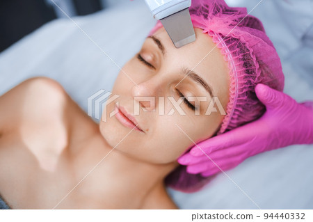Beautician cosmetologist doing ultrasonic facial cleansing skin with device, professional cosmetic procedure in a beauty clinic salon for client. Skincare and machine cosmetology spa concept Beautician cosmetologist doing ultrasonic facial cleansing skin with device, professional cosmetic procedure in a beauty clinic salon for client. Skincare and machine cosmetology spa concept 94440332
