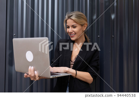 middle-aged woman office worker with a laptop in her hands against a gray wall middle-aged woman office worker with a laptop in her hands against a gray wall 94440538