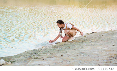 Teenage girl splashes water from the river and laughs Teenage girl splashes water from the river and laughs 94440738