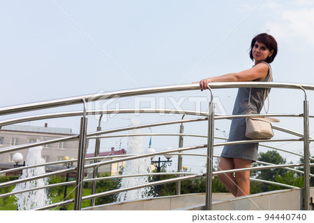 An adult woman stands on a bridge in the city center 94440740