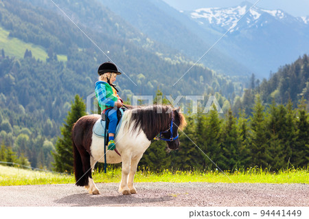 Kids riding pony. Child on horse in Alps mountains 94441449