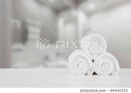 Stacked white spa towels on table against blurred background Stacked white spa towels on table against blurred background 94442353