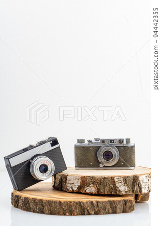Two retro photo cameras on wooden boards. Concept of mens and womens cameras. Vertical shot isolated on white. Two retro photo cameras on wooden boards. Concept of mens and womens cameras. Vertical shot isolated on white. 94442355
